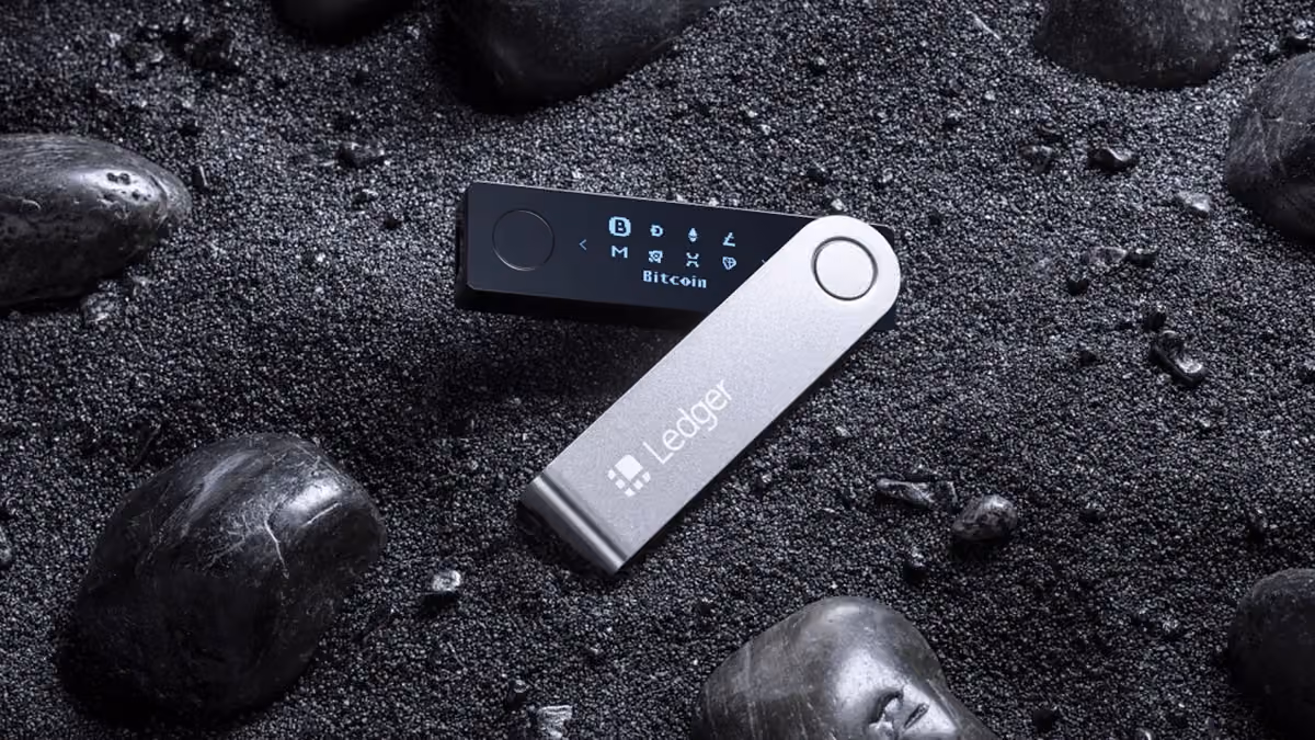 Ledger hardware wallet with its silver swivel cover open, resting on dark stones